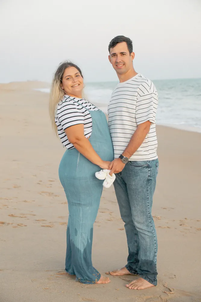 Casal grávido na praia com sapatinhos de bebé