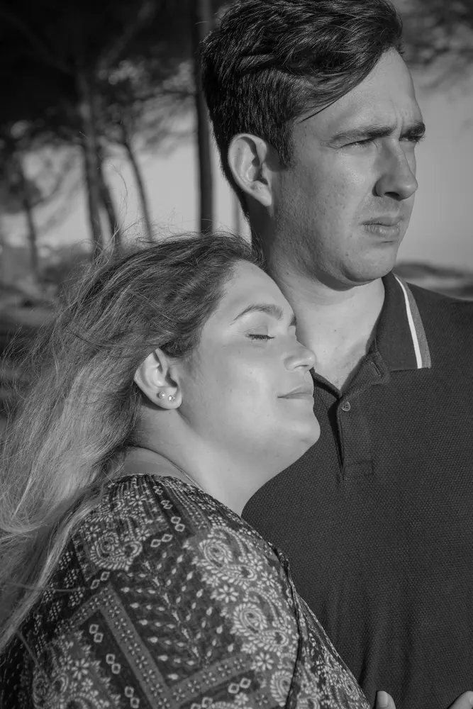 Retrato a preto e branco de um casal num pinhal, com o cabelo ao vento