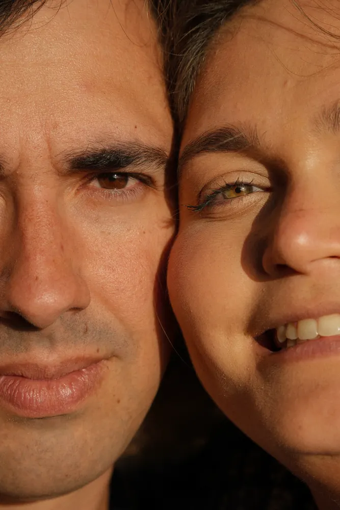 Grande plano de um casal com os rostos encostados, iluminados pelo sol baixo