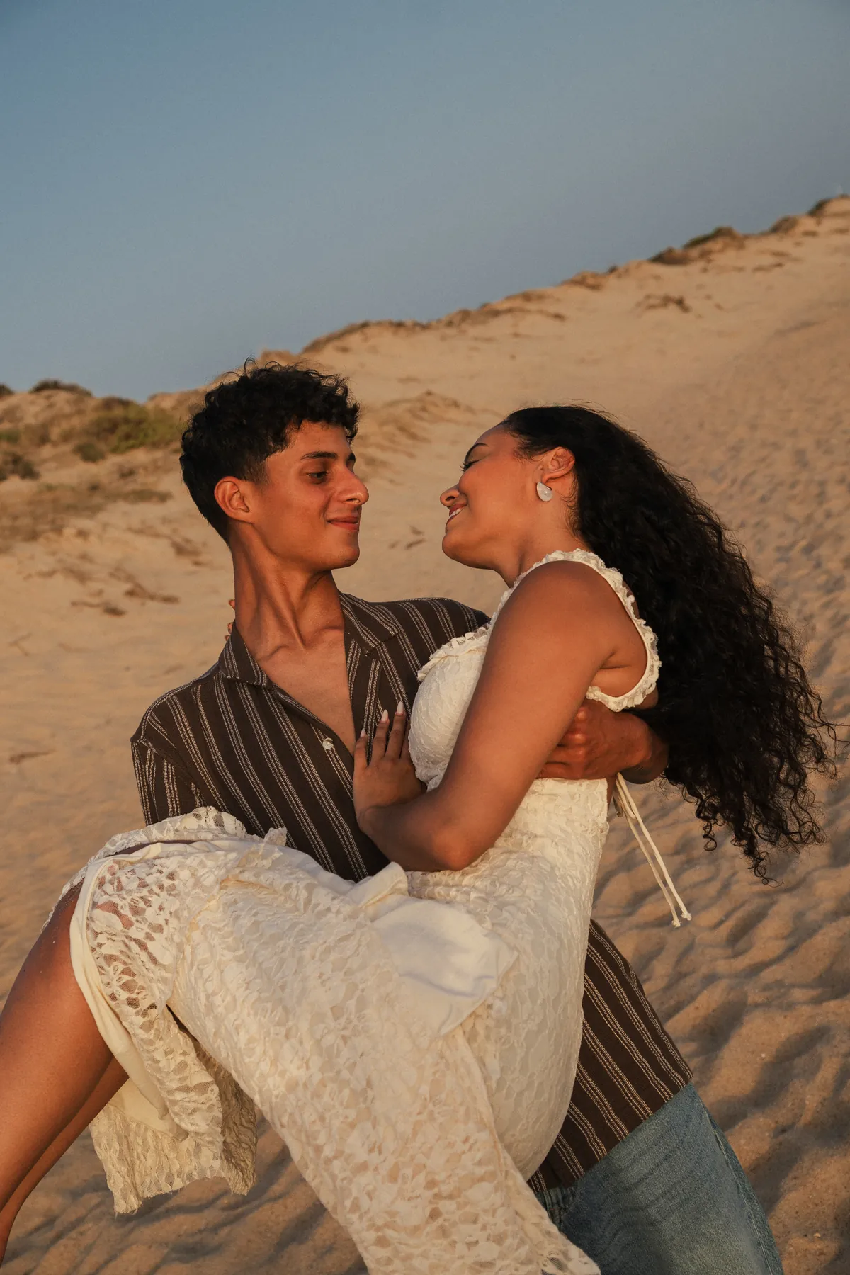 Noivo pega a noiva ao colo numa duna ao pôr do sol durante um elopement no Algarve