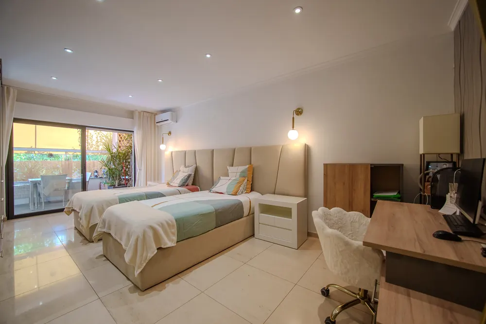 Quarto duplo de uma villa no Algarve com camas individuais, candeeiros dourados e saída para o terraço