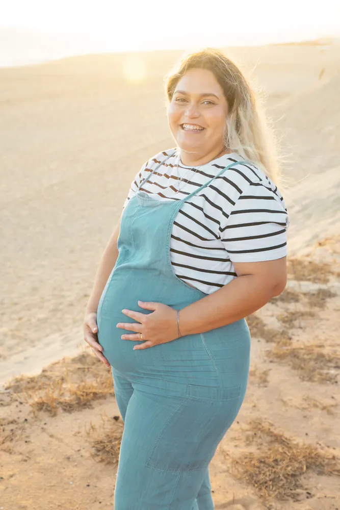 Mulher grávida a sorrir numa duna ao pôr do sol numa praia do Algarve